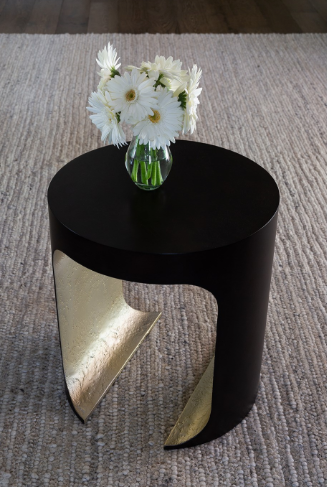 Black side table with decorative leg and vase of flowers on carpet.
