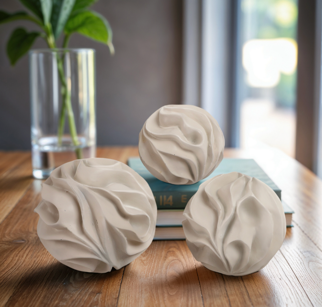 Three textured ceramic balls on a wooden surface with a plant and books in the background.