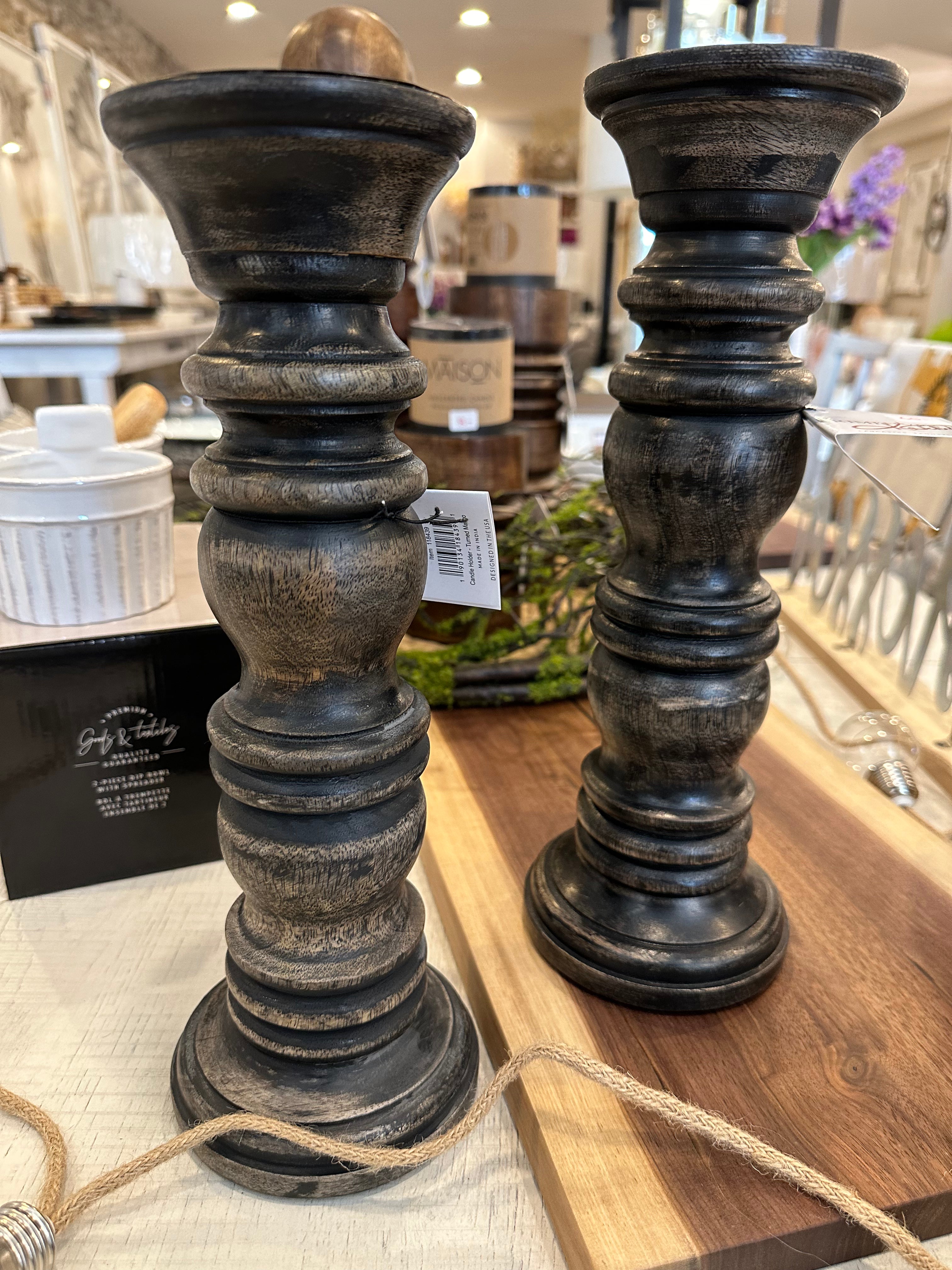 Two weathered black wooden candle holders with a cylindrical shape and a rope in the center, displayed on a wooden surface.