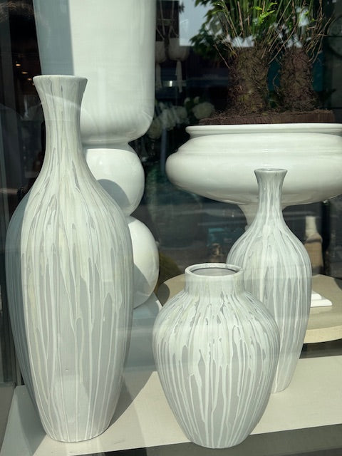 A set of white and gray large vases of different sizes displayed in a storefront window, with one vase containing a green plant.