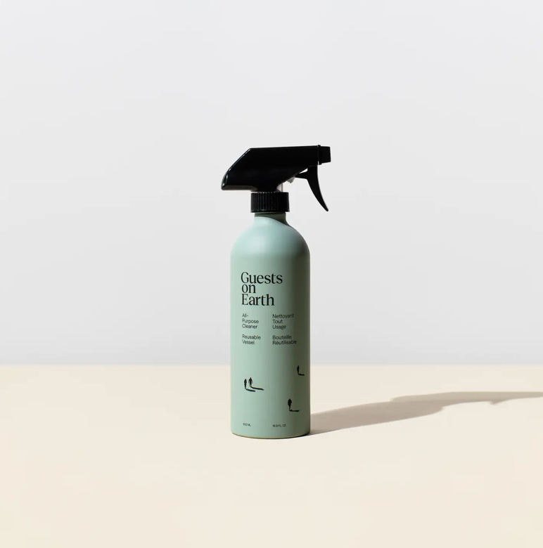 Spray bottle labeled 'Guests on Earth' on a light beige background